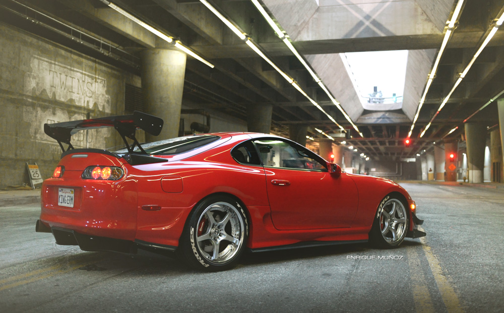 A red performance car beneath city overpasses at night